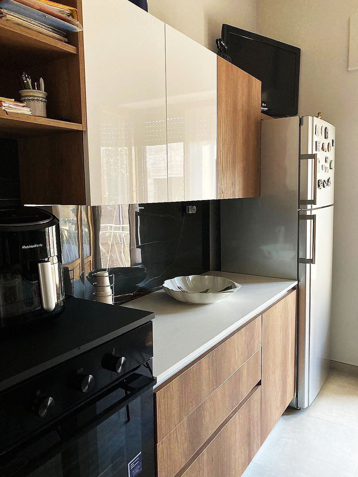 Cucina moderna con mobili bianchi e color legno, piano di lavoro bianco e forno nero.