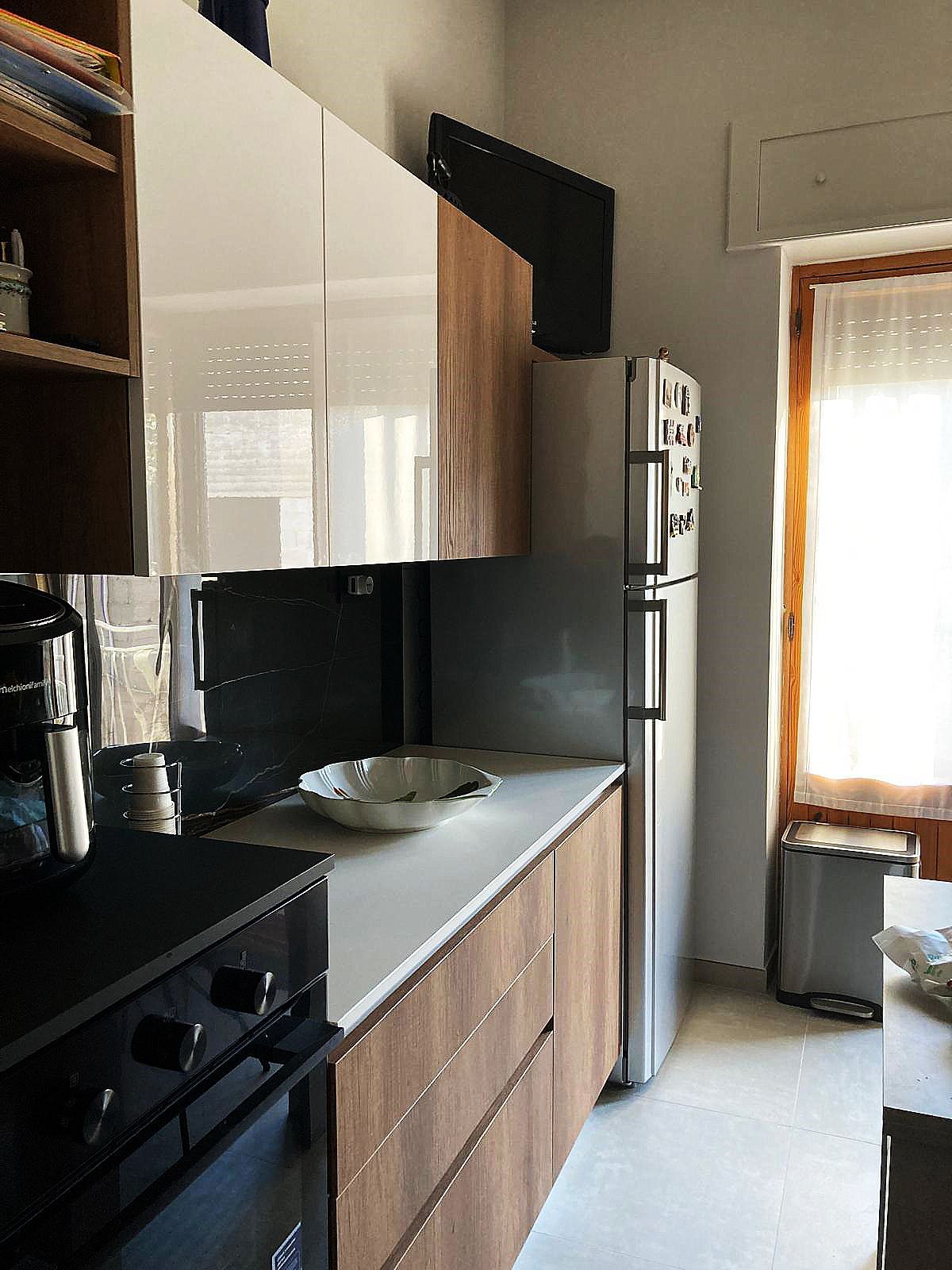 Cucina con mobili bianchi e in legno, frigorifero in acciaio inox e finestra con luce naturale.