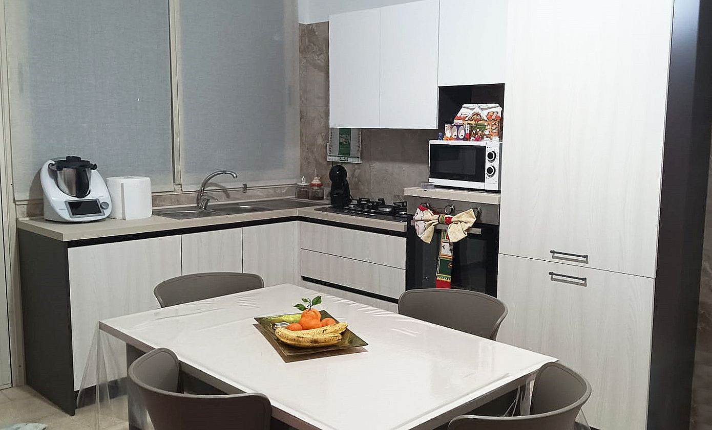 Una cucina moderna con mobili bianchi, ripiani grigio chiaro e un tavolo da pranzo con sedie.