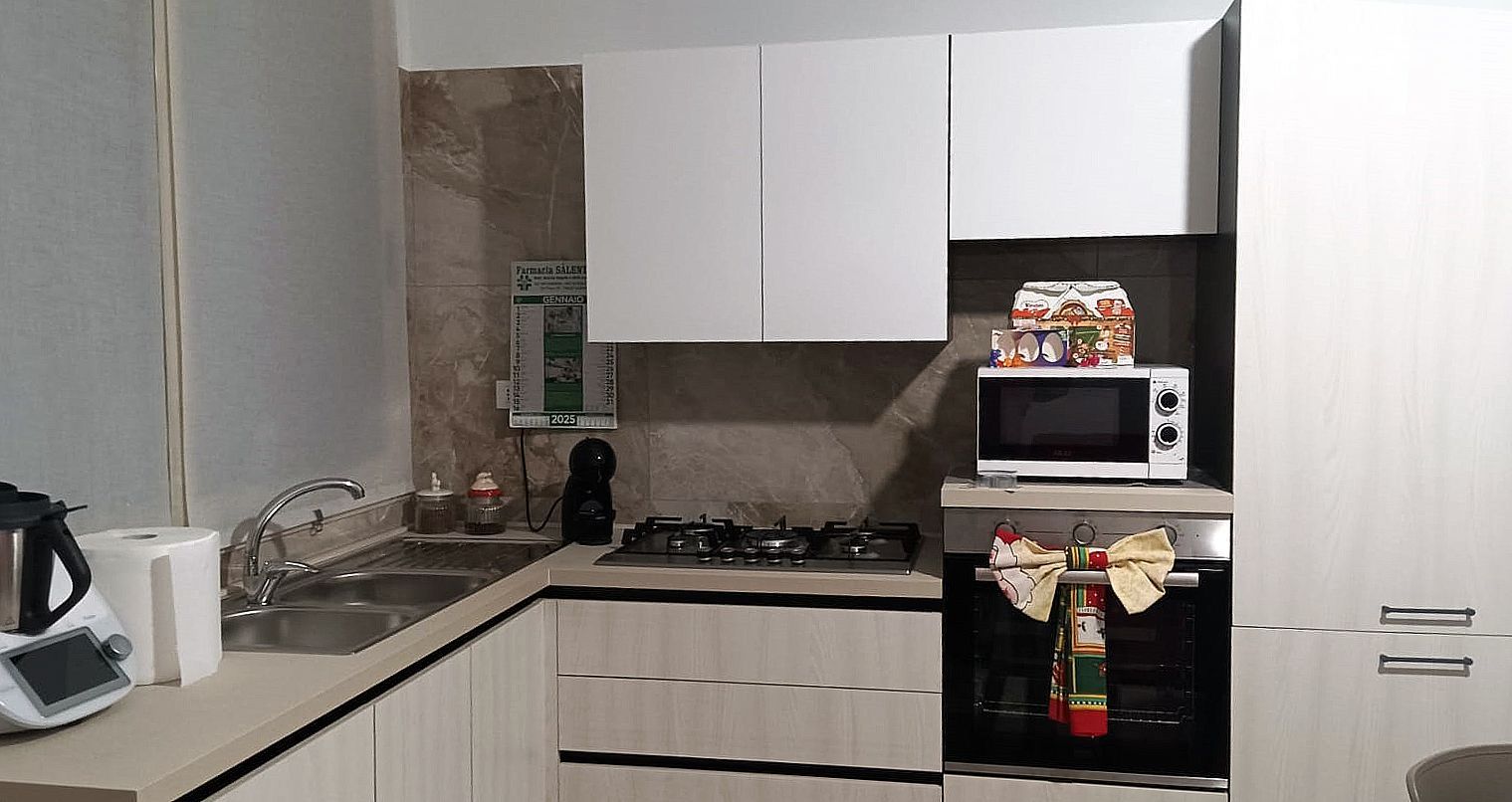Una cucina moderna con mobili bianchi, elettrodomestici in acciaio inossidabile e un piano di lavoro beige.
