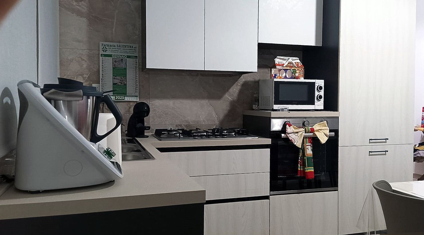 Cucina con mobili bianchi, elettrodomestici e un Bimby.