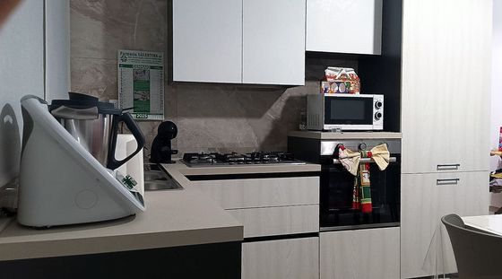 Cucina con mobili bianchi, elettrodomestici e un Thermomix sul bancone.