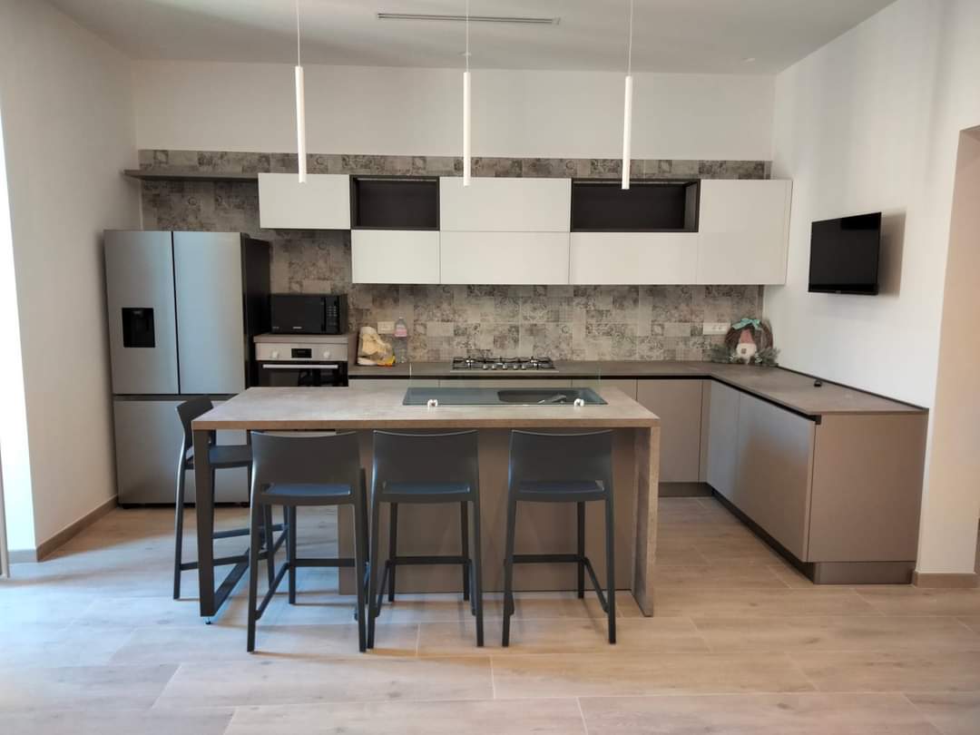 Cucina moderna con pavimento in legno chiaro, isola con sgabelli ed elettrodomestici in acciaio inossidabile.