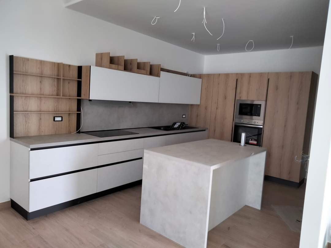 Cucina moderna con mobili bianchi e in legno, isola ed elettrodomestici da incasso.