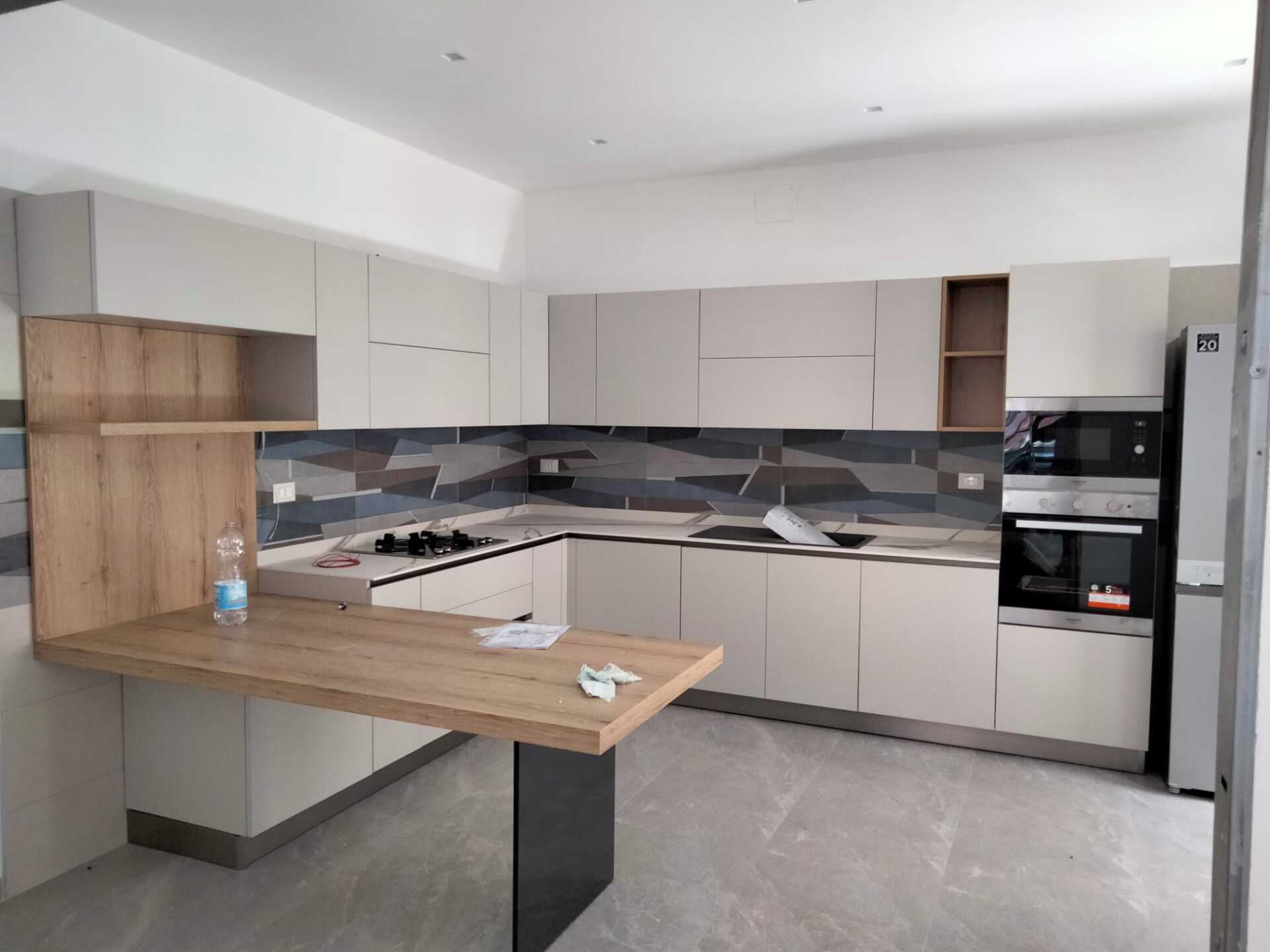 Cucina moderna con mobili grigio chiaro, piano di lavoro in legno e paraschizzi grigio-blu.