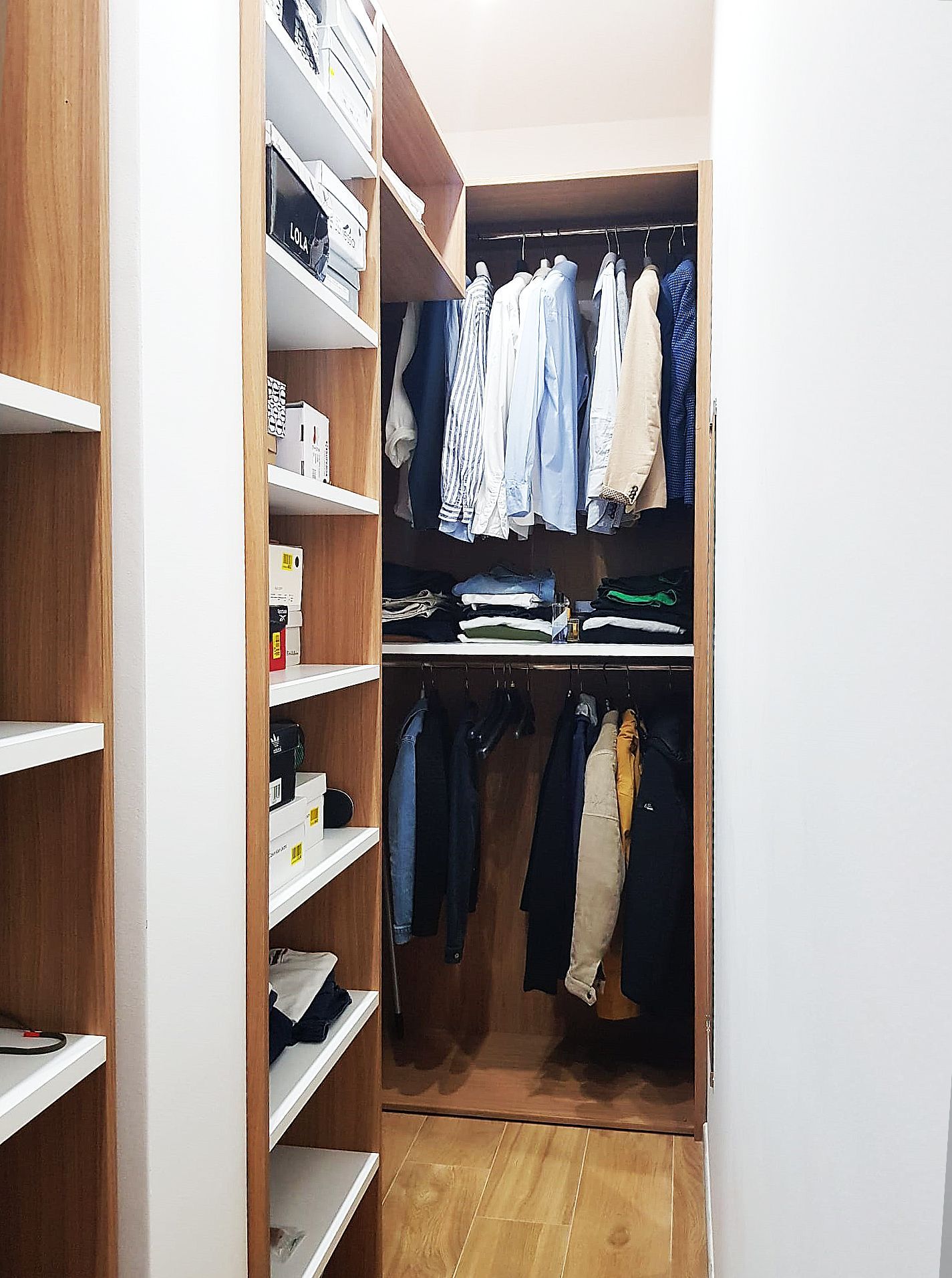 Cabina armadio con ripiani in legno e appendiabiti. Camicie e pantaloni sono appesi all'interno.