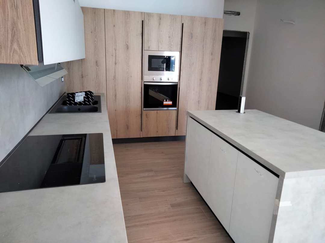 Cucina moderna con mobili in legno chiaro, ripiani grigi e isola.