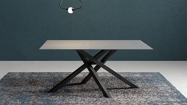Tavolo da pranzo quadrato grigio con gambe nere incrociate su un tappeto a fantasia.