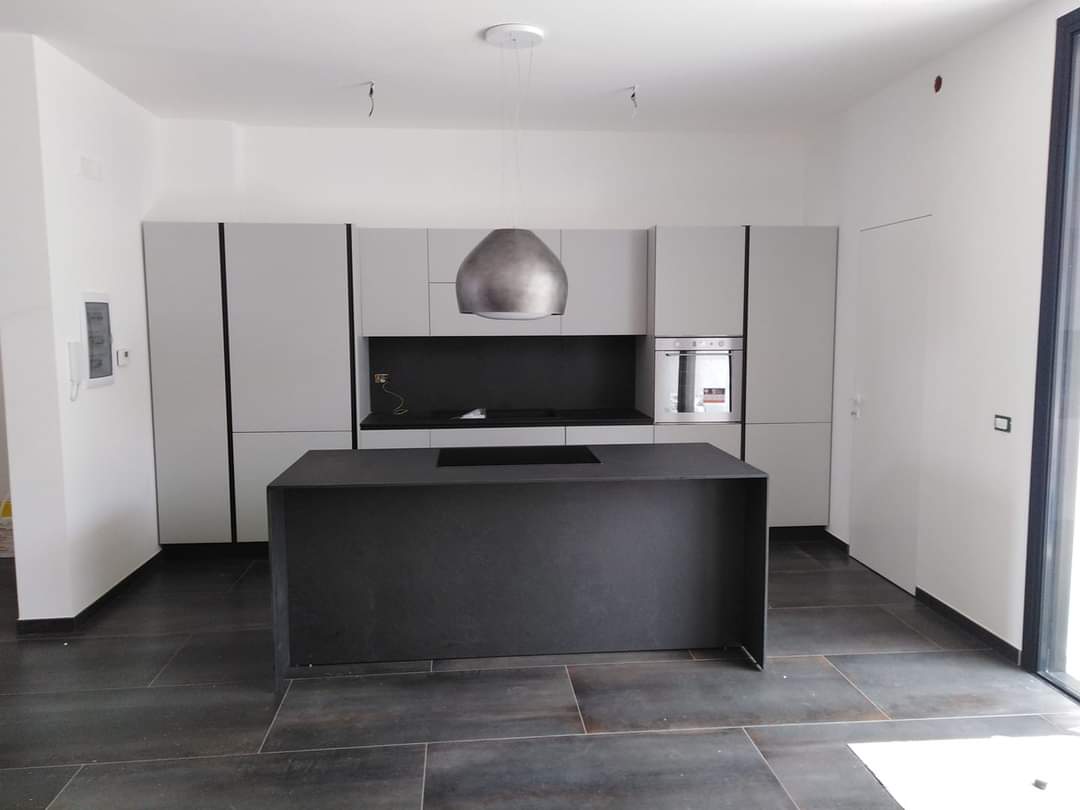 Cucina moderna con mobili grigi, isola scura e cappa in acciaio inossidabile.