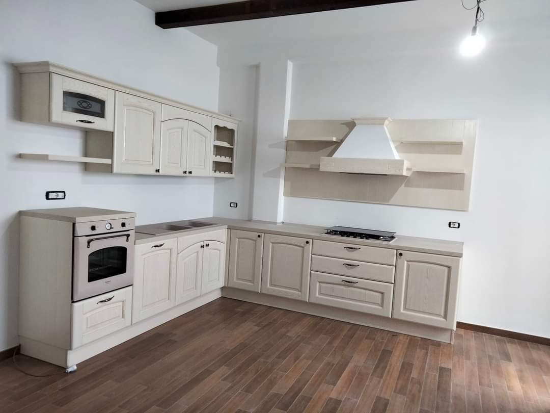 Mobili da cucina ed elettrodomestici color crema in una stanza con pavimento in legno e cappa bianca.