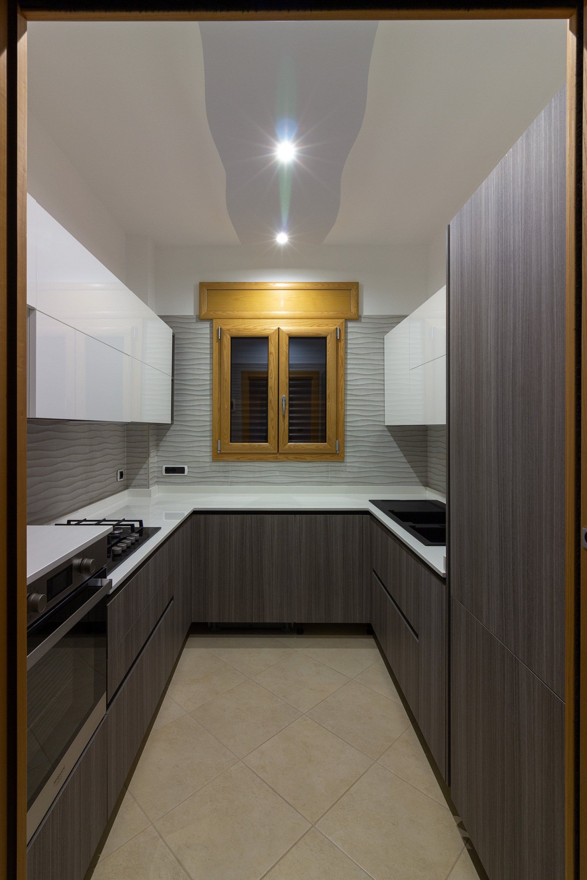 Cucina moderna a U con mobili in legno e grigi, ripiani bianchi, paraschizzi in piastrelle e una finestra.