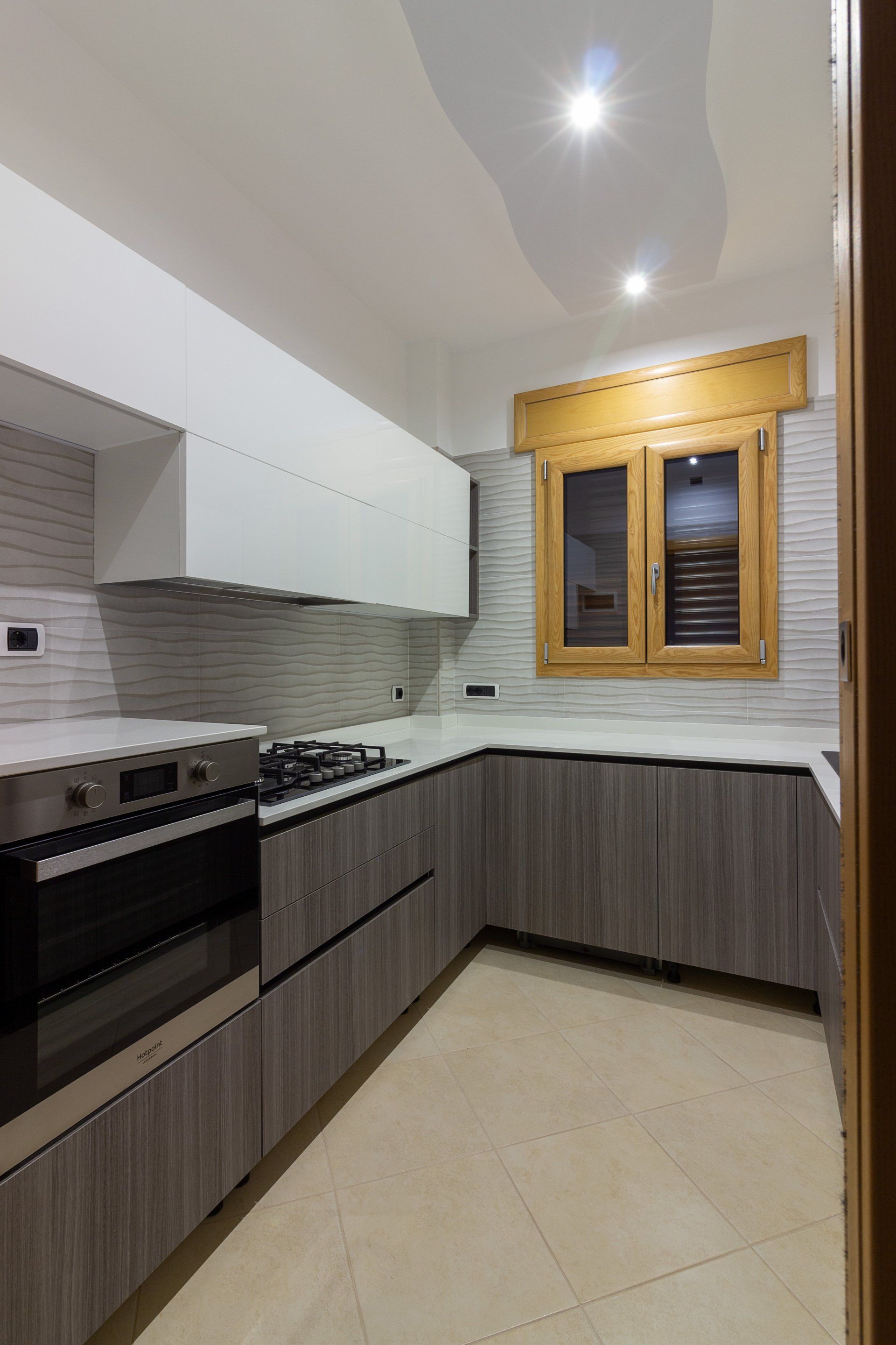 Cucina moderna con mobili grigi, piano di lavoro bianco e cornice della finestra in legno chiaro.