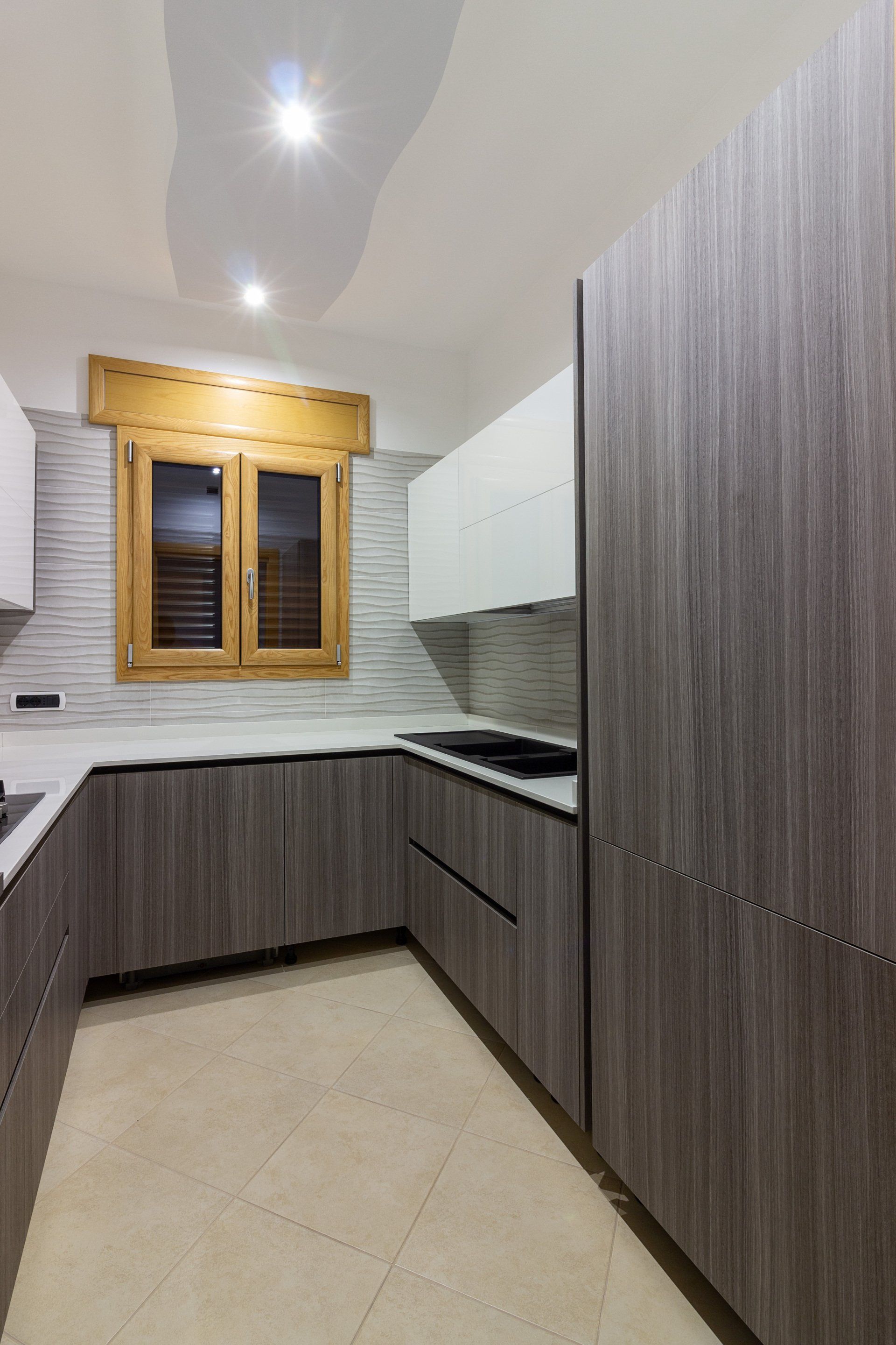 Cucina moderna con mobili in legno grigio, ripiani bianchi e una finestra con cornice in legno.