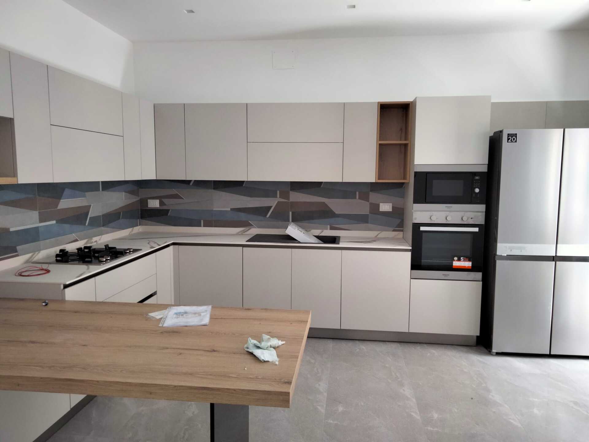 Cucina moderna con mobili chiari, isola in legno, paraschizzi piastrellato ed elettrodomestici in acciaio inossidabile.