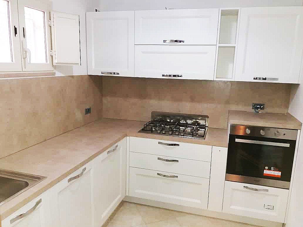 Mobili da cucina e ripiani bianchi con forno, piano cottura e lavello integrati.