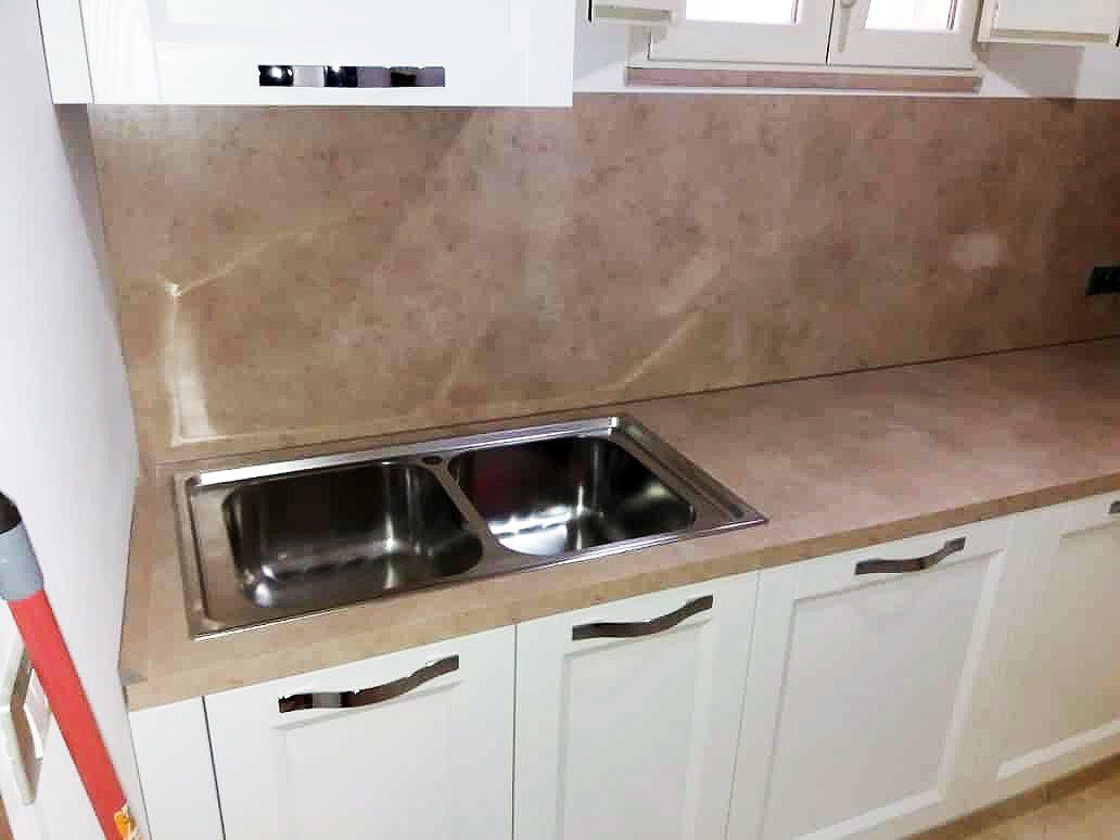Cucina con doppio lavello in acciaio inox, mobili bianchi, piano di lavoro e paraschizzi beige.