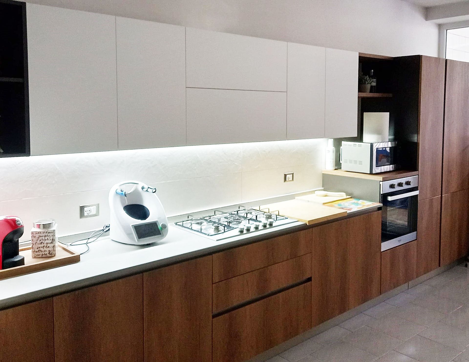 Cucina moderna con mobili bianchi e in legno, elettrodomestici in acciaio inossidabile e piano di lavoro con piano cottura integrato.