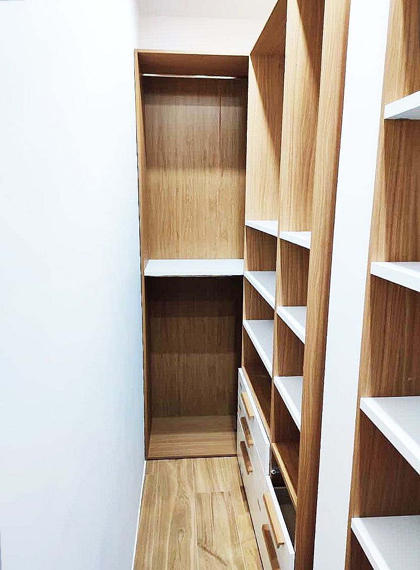 Cabina armadio con ripiani e cassetti in legno e pareti bianche.
