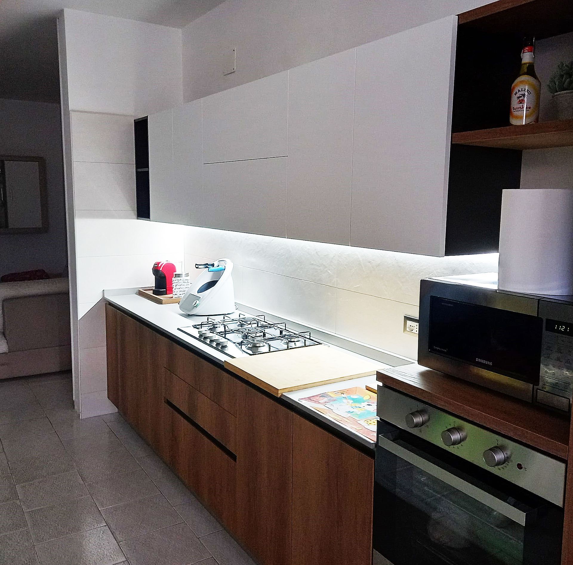 Cucina con mobili bianchi, dettagli in legno ed elettrodomestici: forno, microonde e piano cottura.