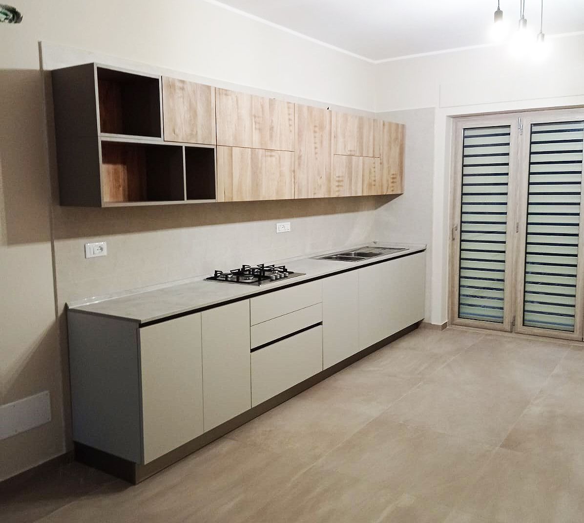 Cucina moderna con mobili grigi, pensili in legno e piano cottura a gas.