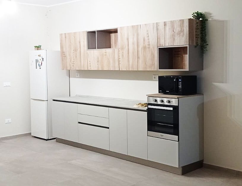 Cucina moderna con mobili grigio chiaro, pensili color legno e frigorifero bianco.