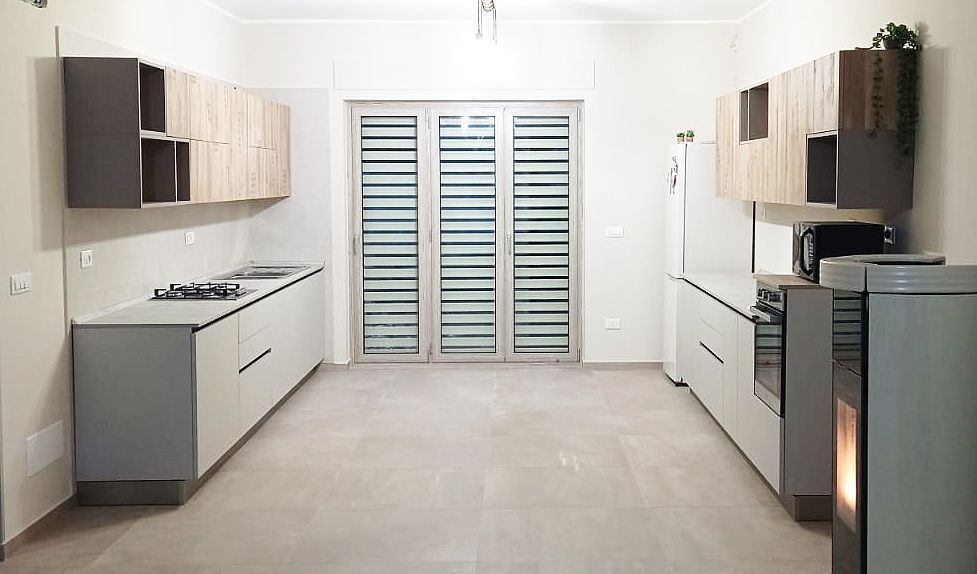 Cucina moderna con mobili grigio chiaro, elettrodomestici in acciaio inossidabile e ampie finestre.