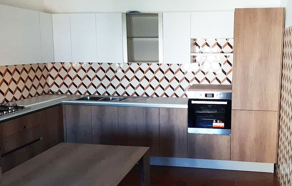 Cucina con mobili marroni e bianchi, paraschizzi piastrellato, forno, fornelli e tavolo.