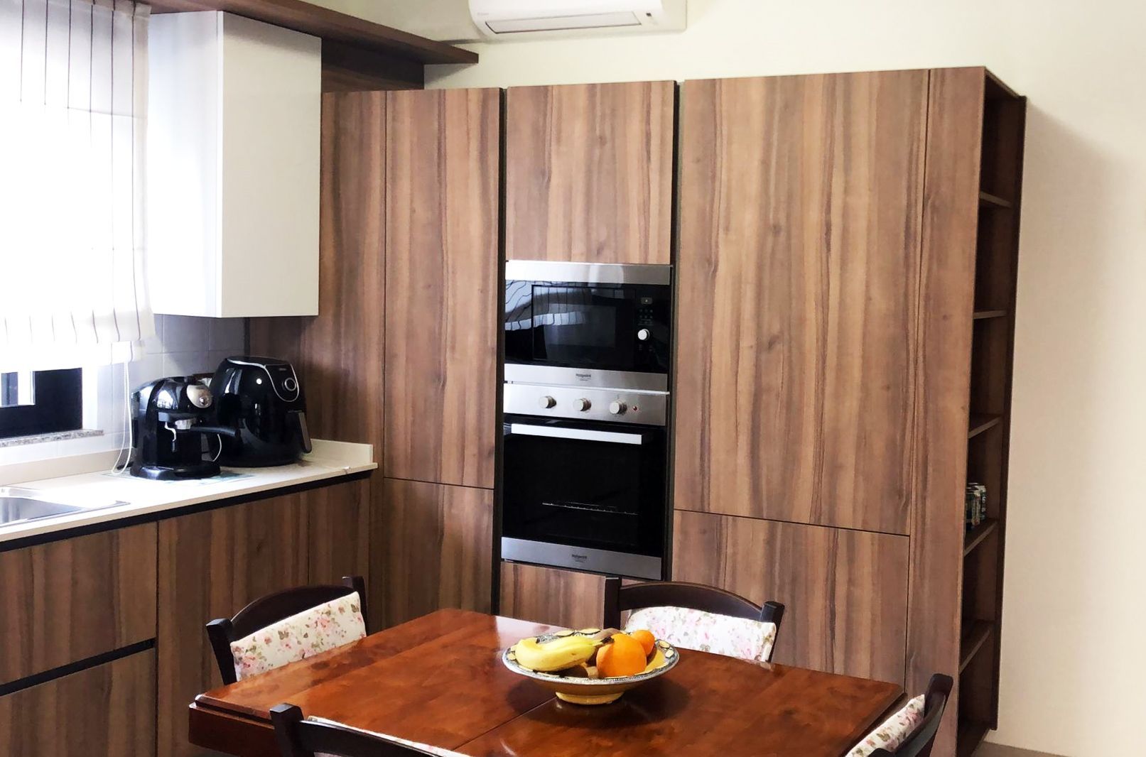 Cucina moderna con mobili in legno, forno incorporato e tavolo da pranzo con frutta.