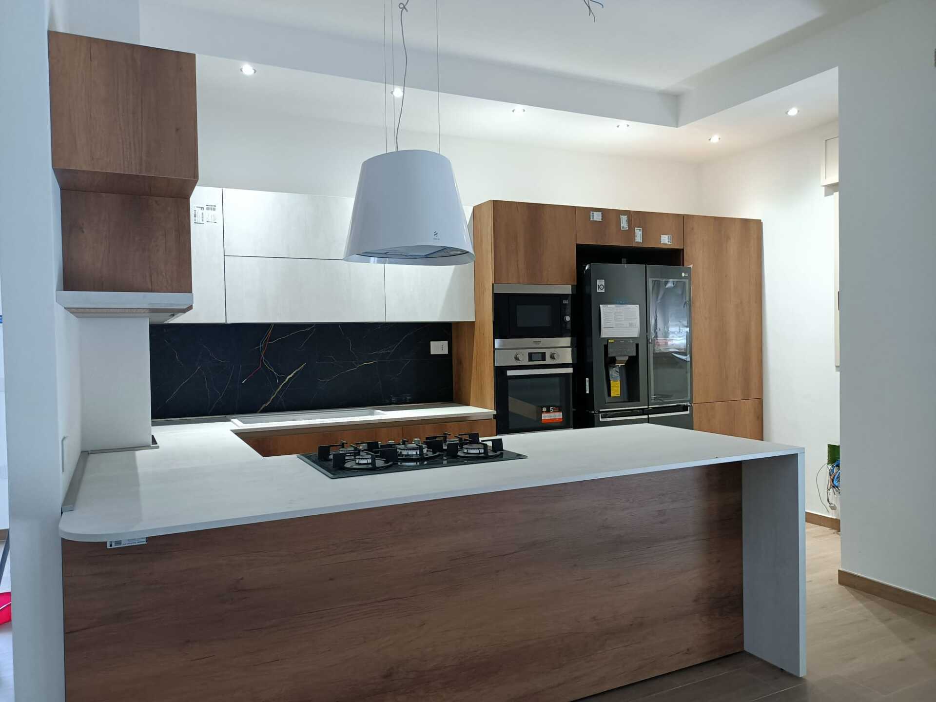 Cucina moderna con piano di lavoro bianco, mobili in legno e paraschizzi nero.