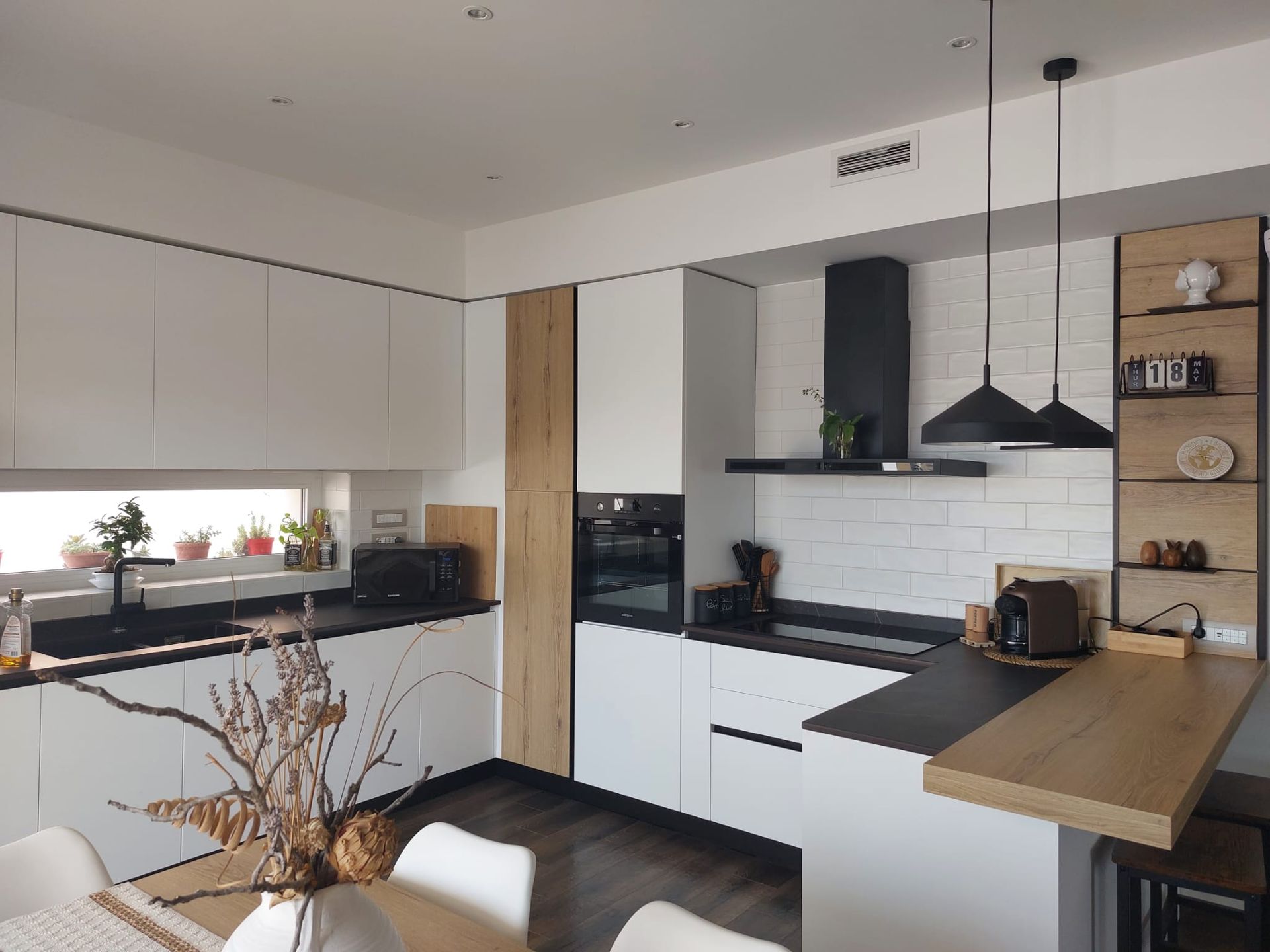 Cucina moderna con mobili bianchi, ripiani scuri e dettagli in legno.
