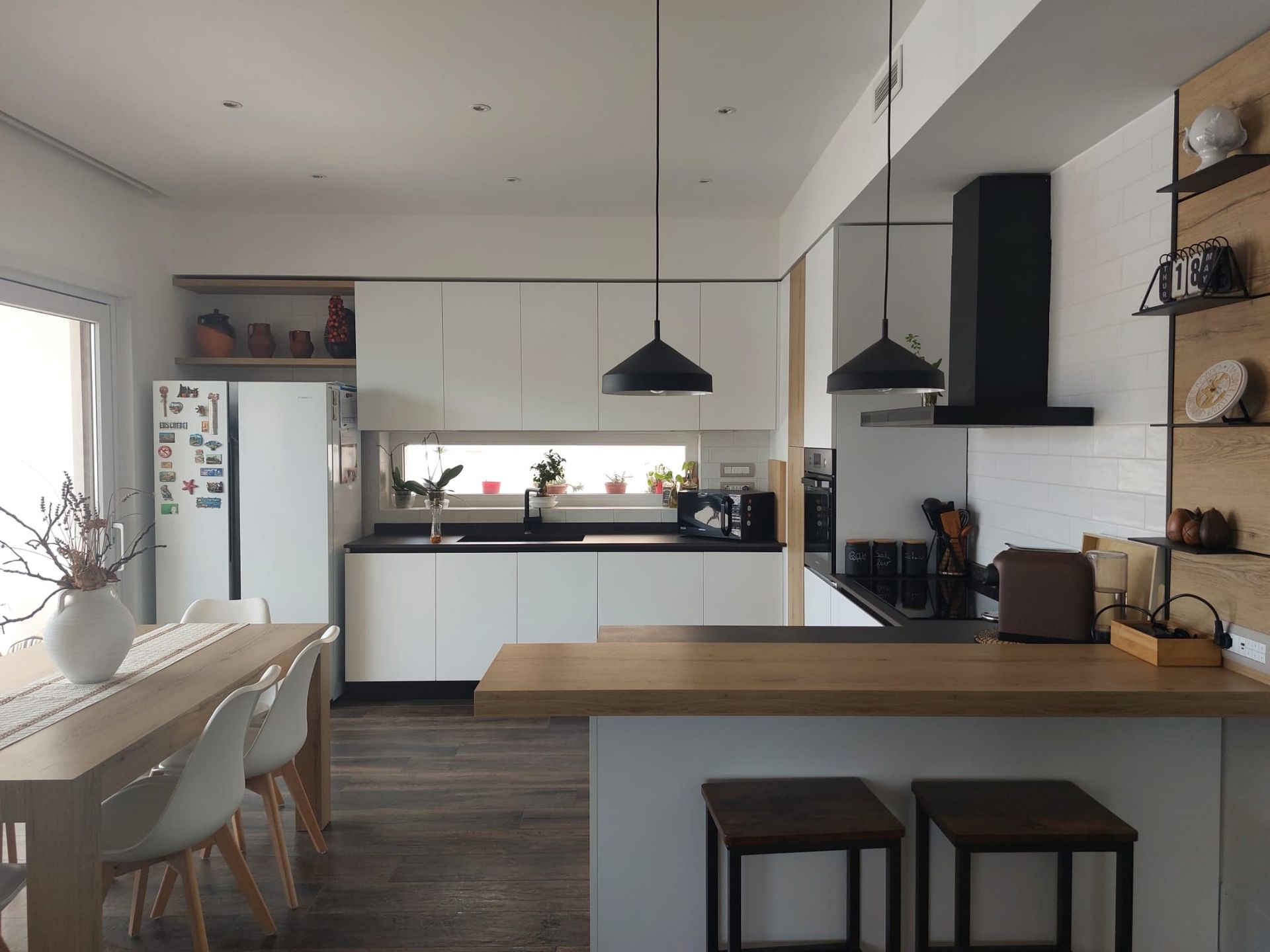 Cucina moderna con mobili bianchi, dettagli in legno, ripiani neri e lampade a sospensione.