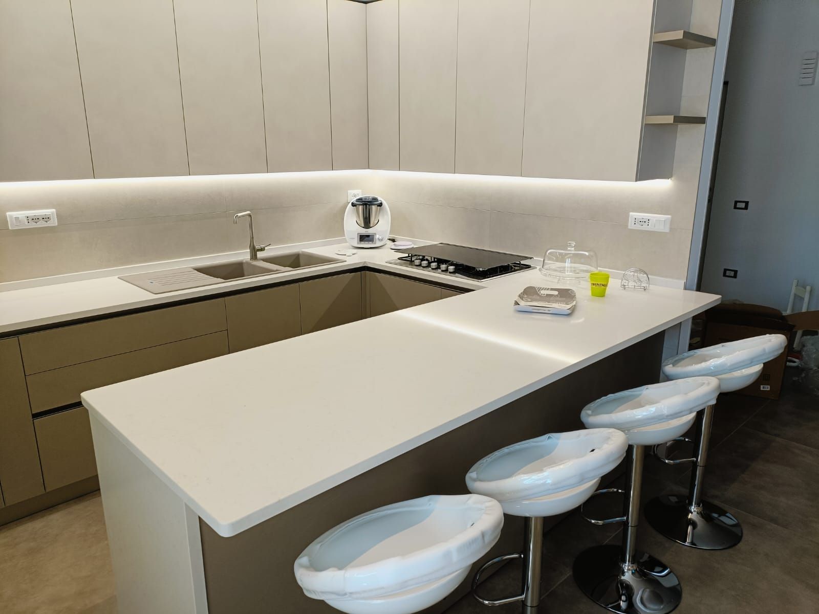 Cucina moderna con bancone per la colazione, ripiani bianchi, mobili chiari e sgabelli da bar.