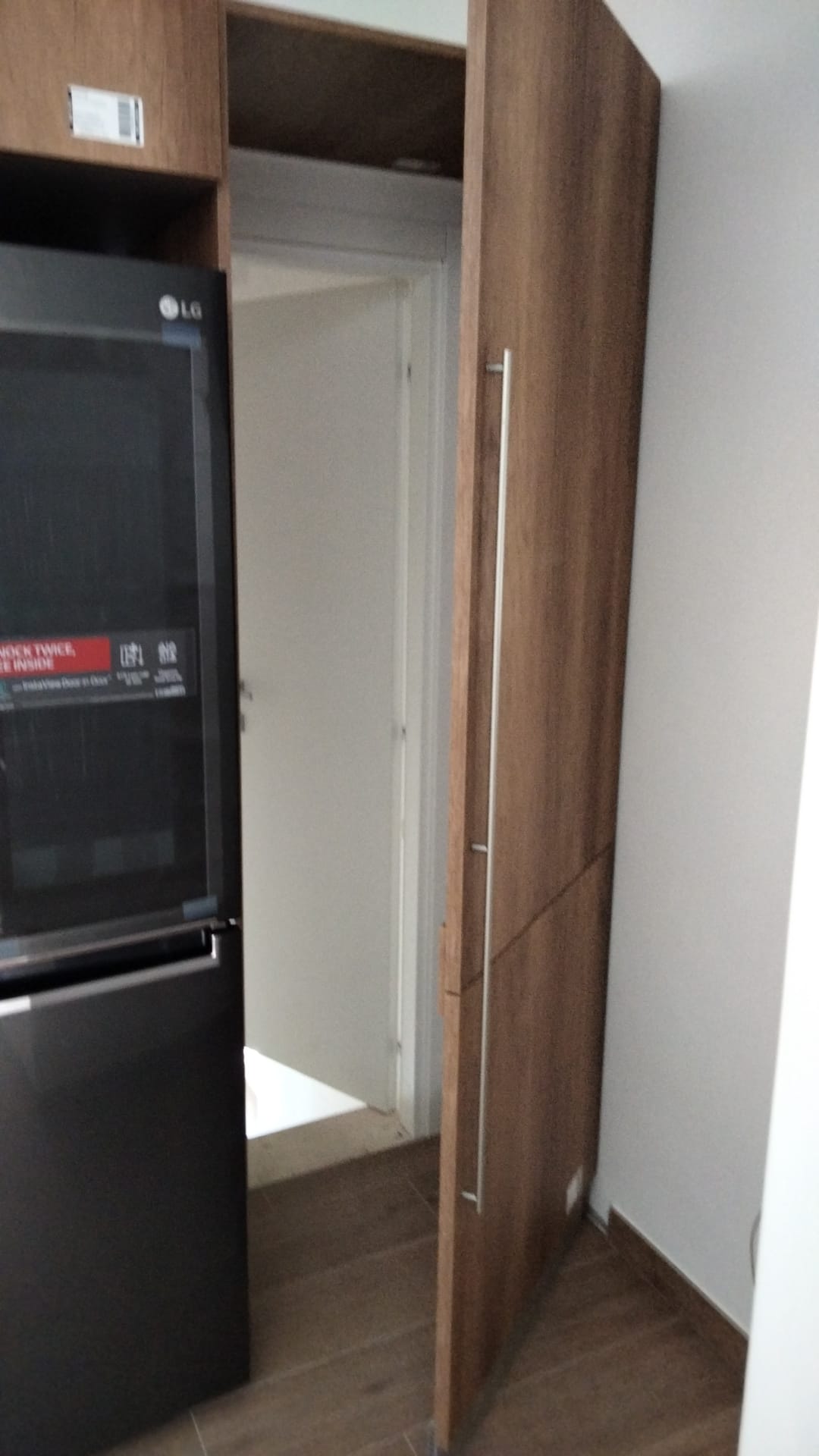 Porta della dispensa socchiusa accanto a un frigorifero nero. Mobili in legno con maniglie argentate. Porta interna.