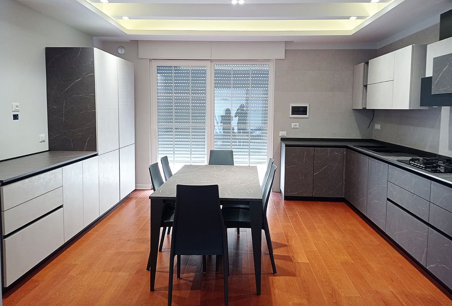 Cucina moderna con pavimenti in legno, mobili grigi e tavolo da pranzo.