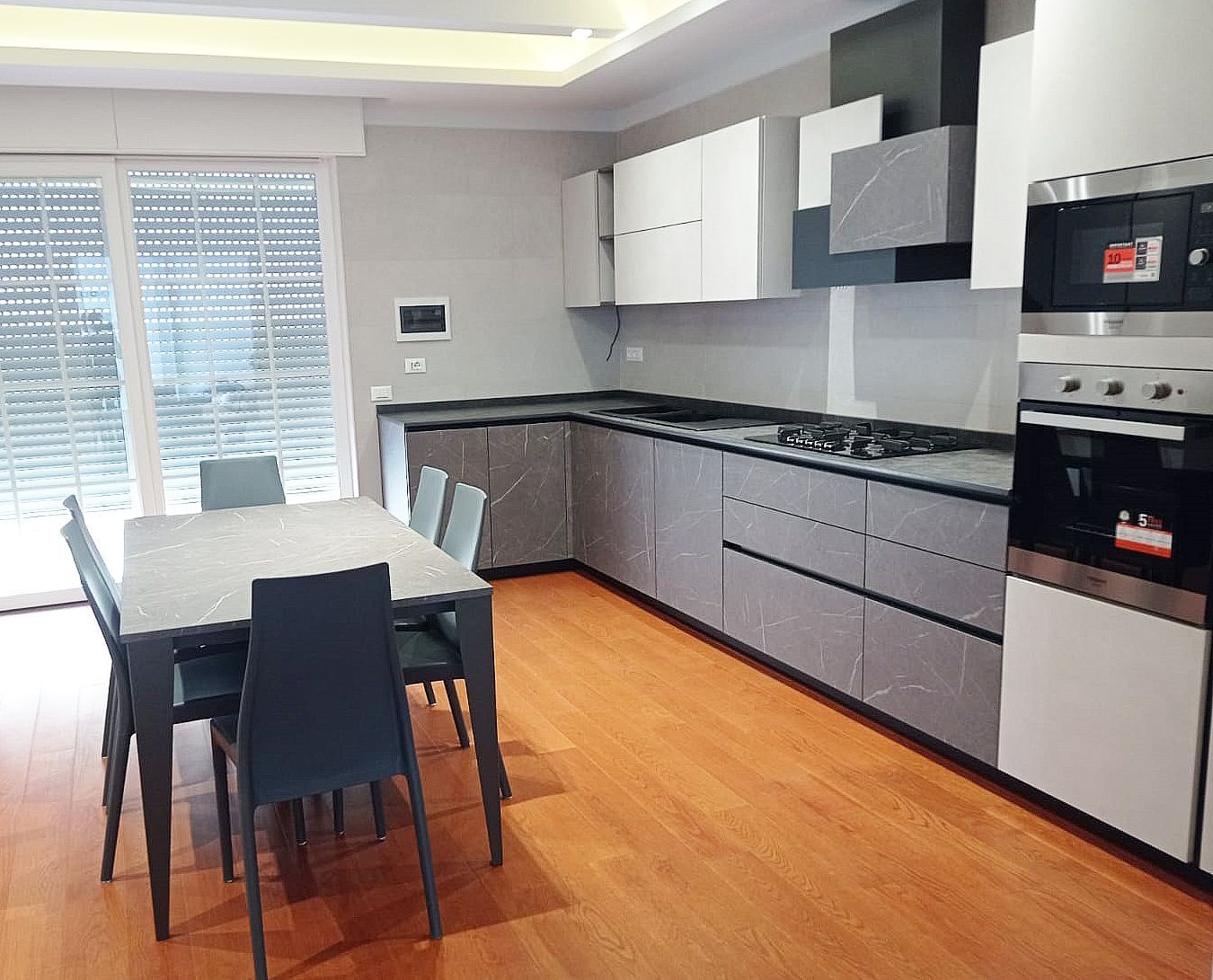 Cucina moderna con mobili grigi e bianchi, elettrodomestici in acciaio inossidabile e tavolo da pranzo.