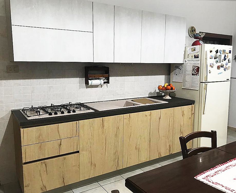 Cucina moderna con pensili bianchi e pensili inferiori effetto legno, piano di lavoro nero e frigorifero bianco.
