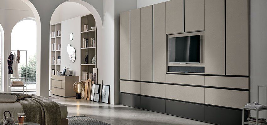 Interno della camera da letto con mobili a muro, TV e archi. Toni neutri e tenui e luce naturale inondano lo spazio.