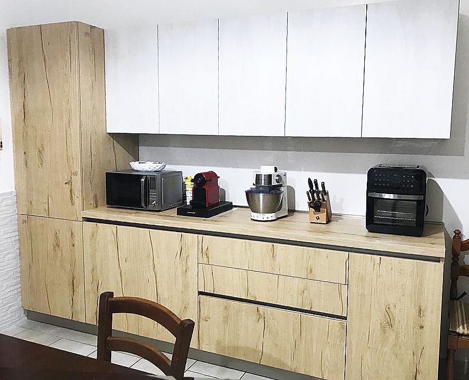 Cucina moderna con mobili in legno chiaro, pensili bianchi, elettrodomestici e una sedia in legno.