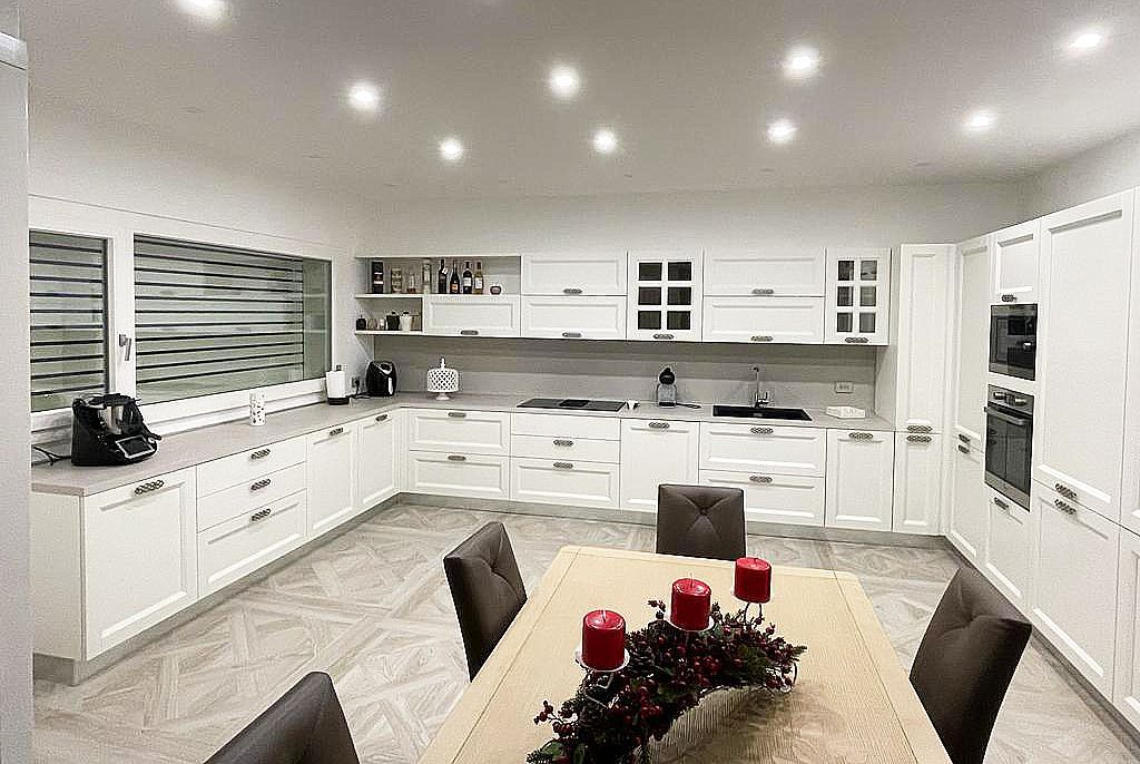 Cucina bianca e luminosa con mobili, elettrodomestici e tavolo da pranzo con candele.
