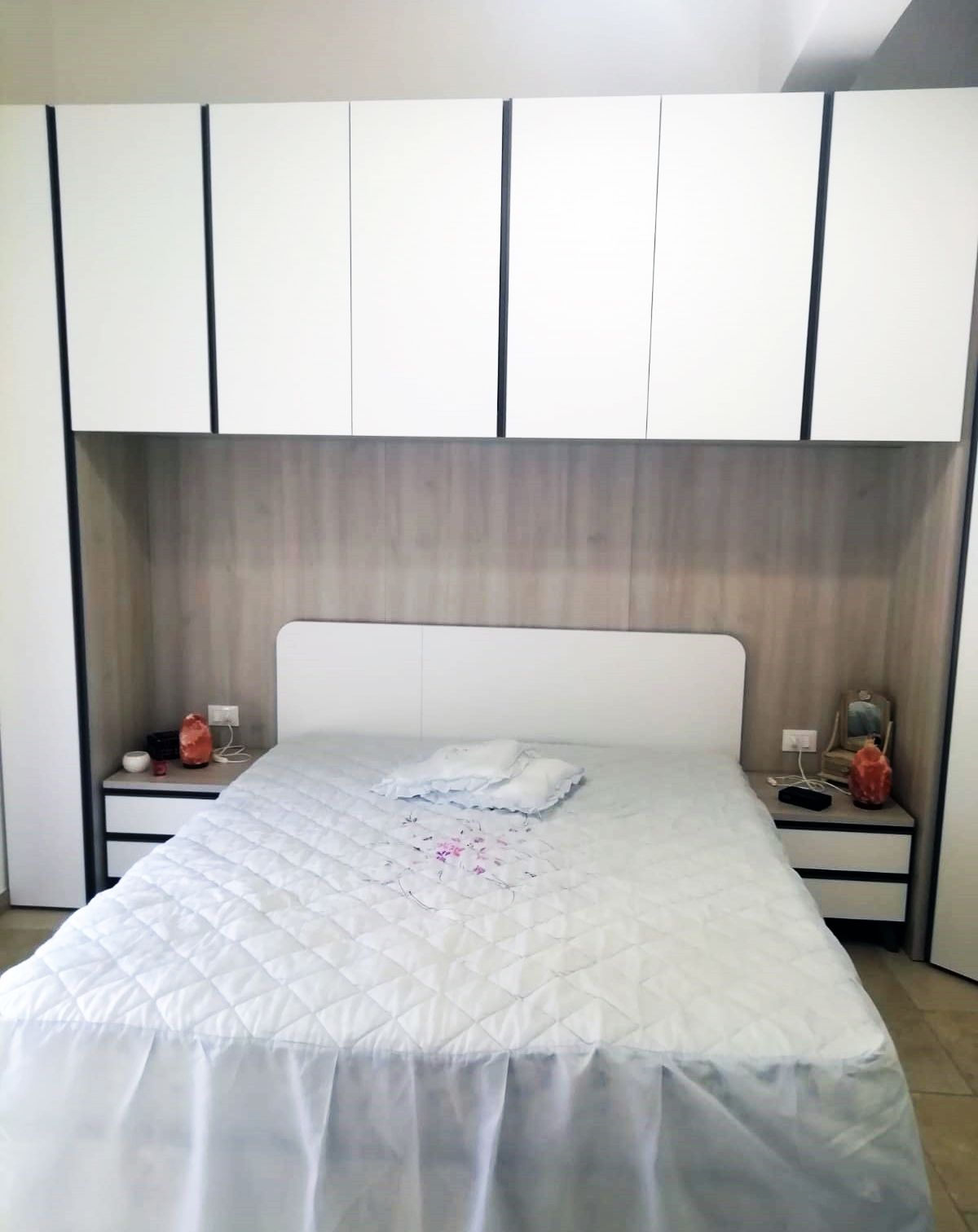 Camera da letto con letto bianco, pensili e comodini.