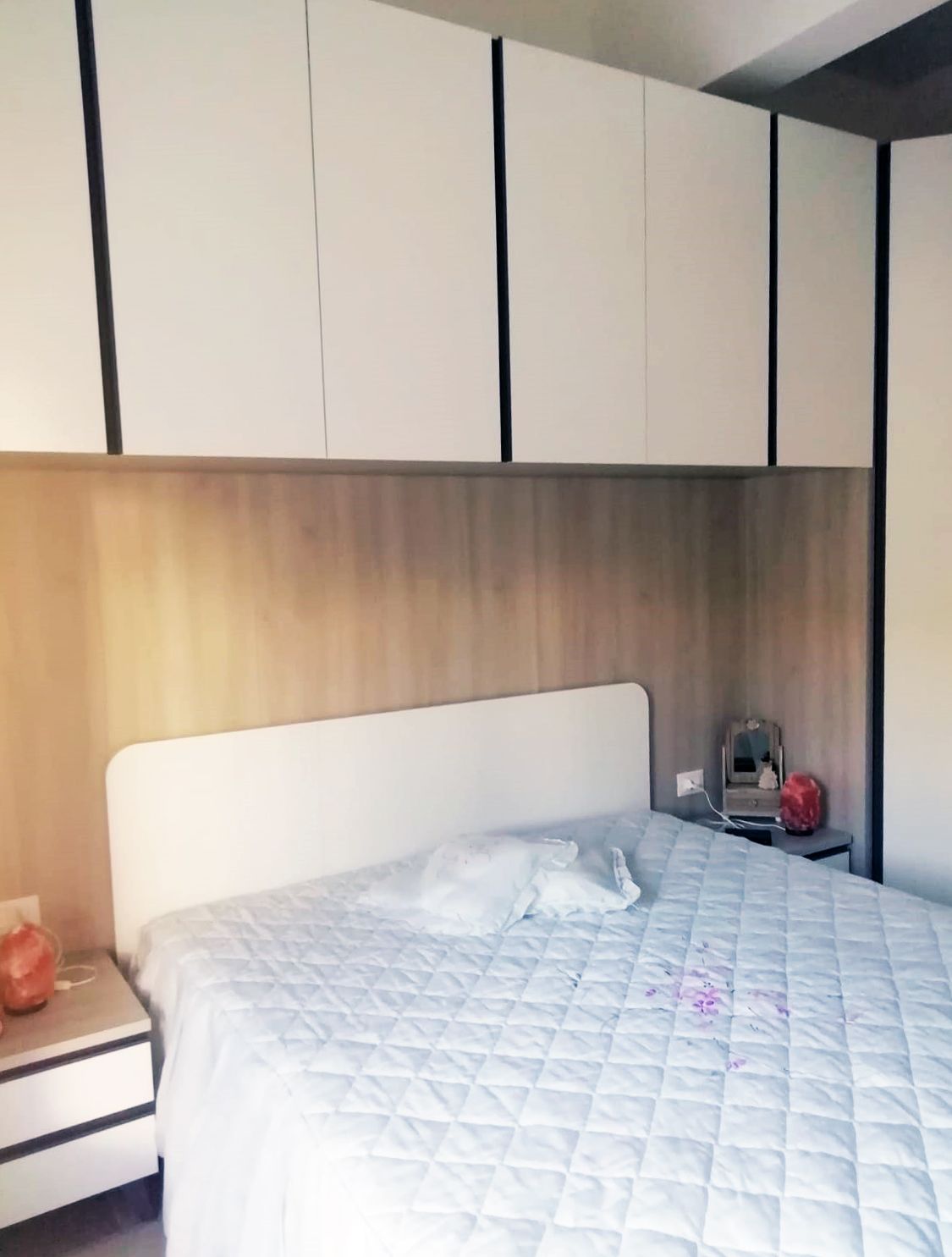 Camera da letto con letto bianco, testiera, comodini e mobili contenitori sospesi.