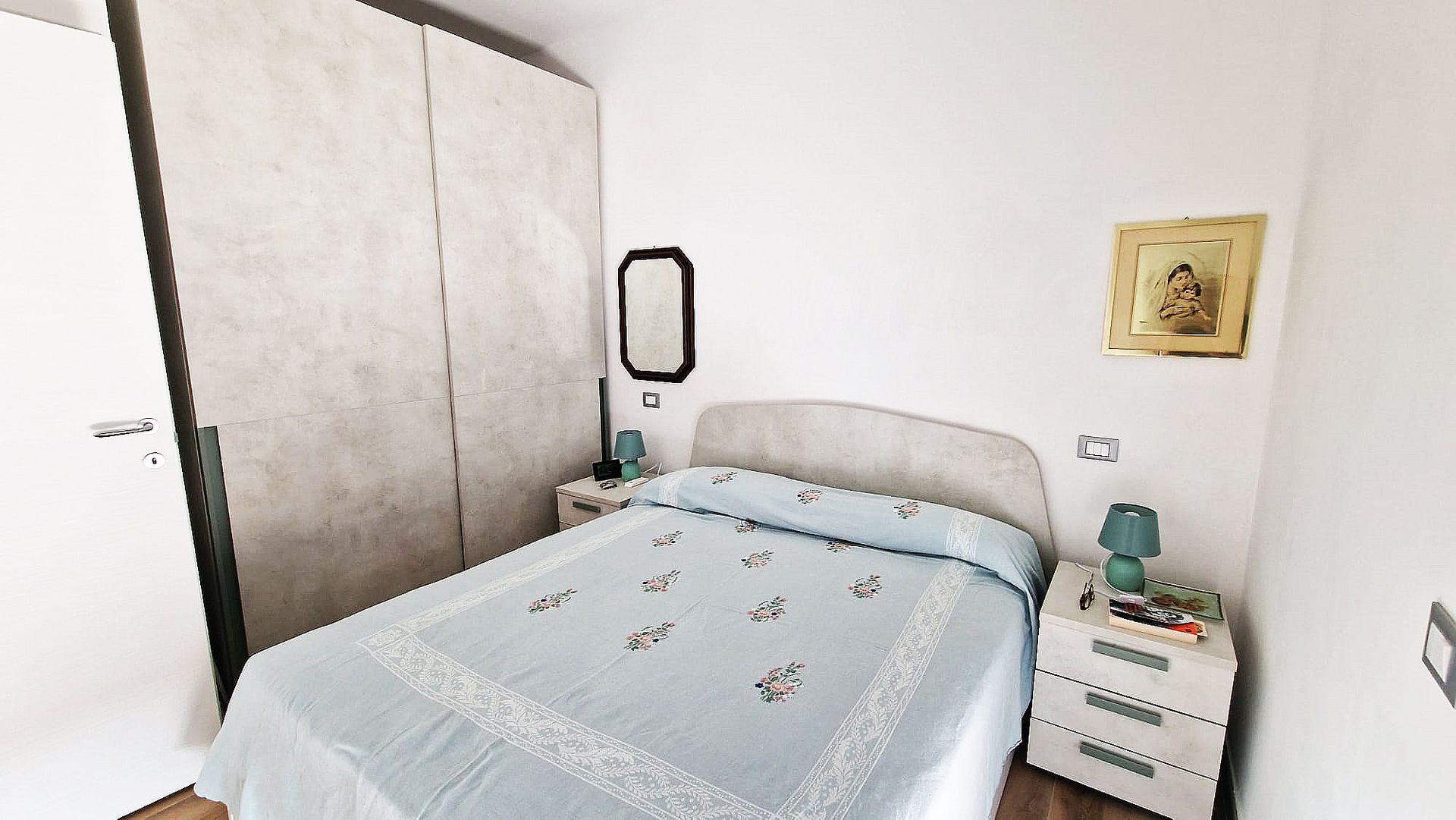 Camera da letto con letto matrimoniale, due comodini, ampio armadio, specchio e opere d'arte alla parete.