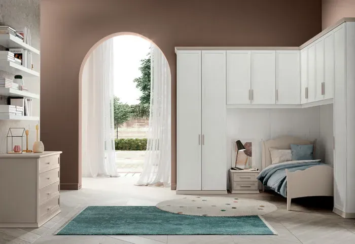 Camera da letto con mobili dai colori chiari, un tappeto blu e una porta ad arco che conduce al giardino.