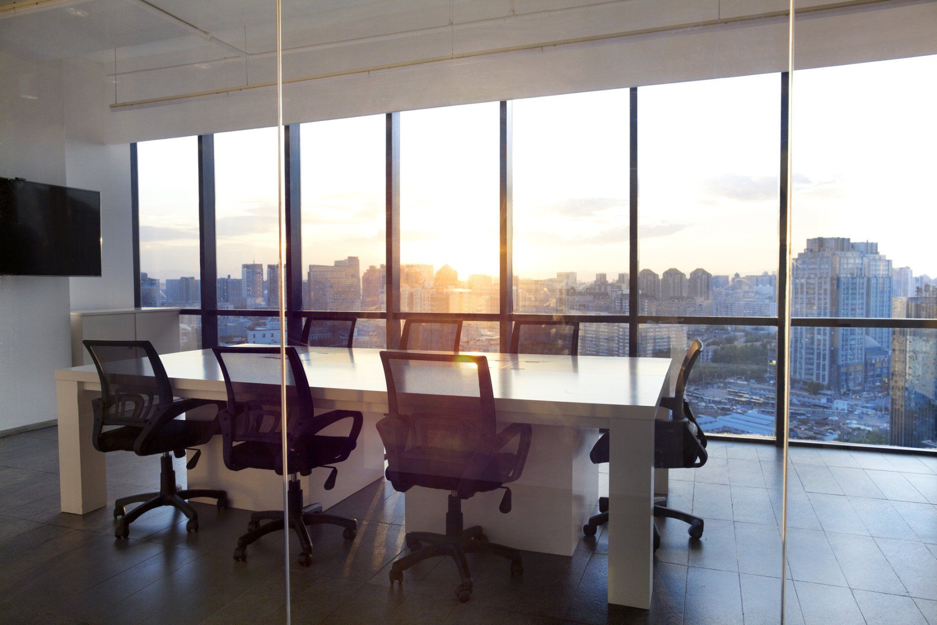 Sala conferenze con ampie finestre che si affacciano sulla città al tramonto. Sedie attorno a un tavolo bianco.