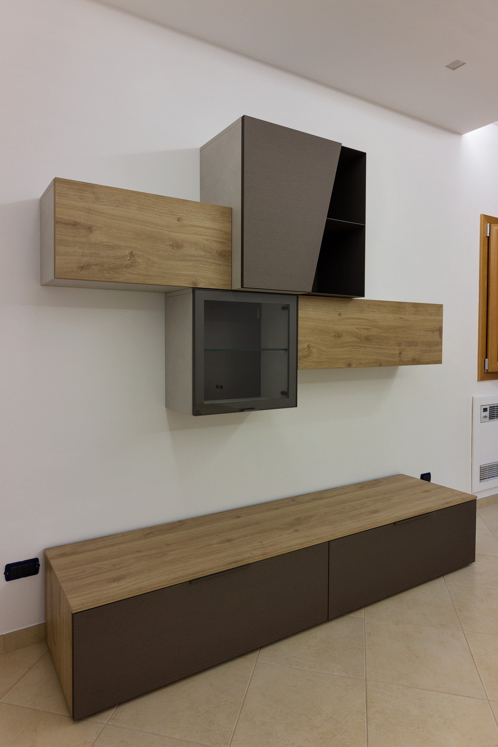 Mobile contenitore moderno a parete: mobili marroni e in legno, anta in vetro, con lunga base su parete bianca.