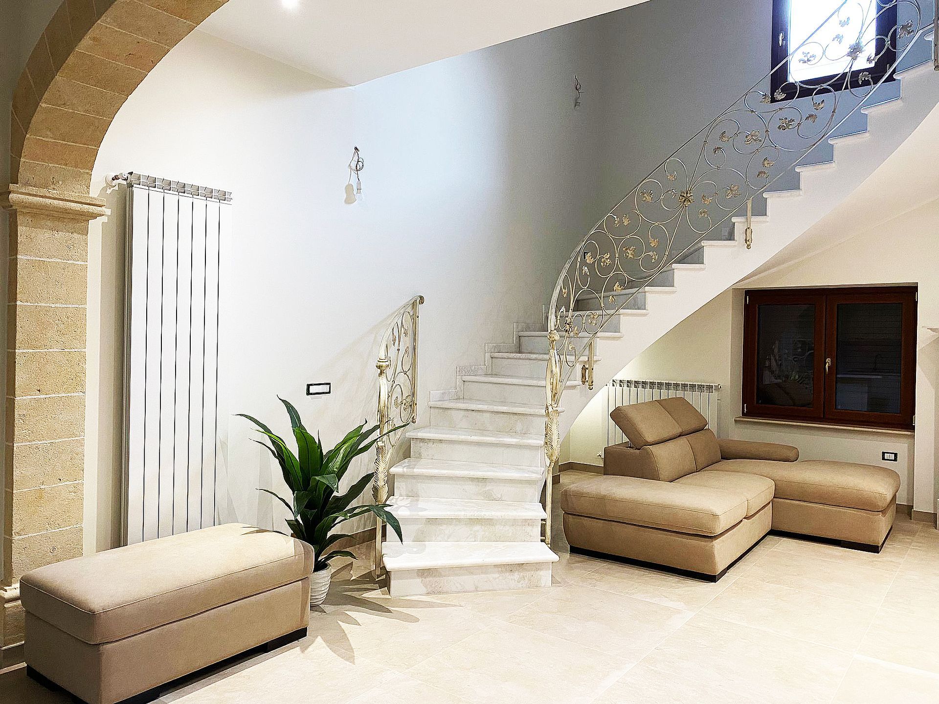 Interni eleganti con scala curva, divano beige e arco in pietra.