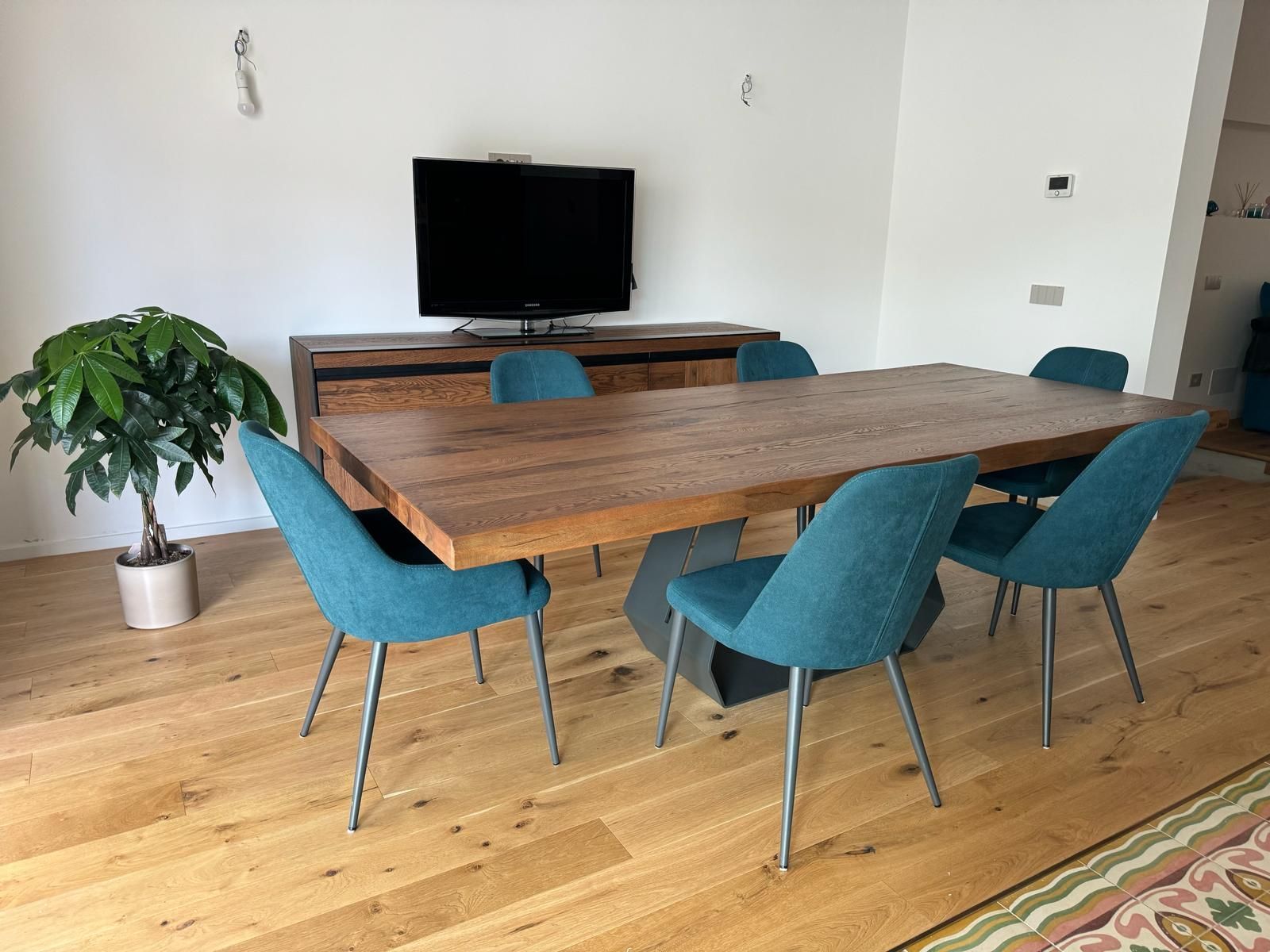 Sala da pranzo con tavolo in legno e sedie color verde acqua, TV su una consolle in legno e pianta in vaso.