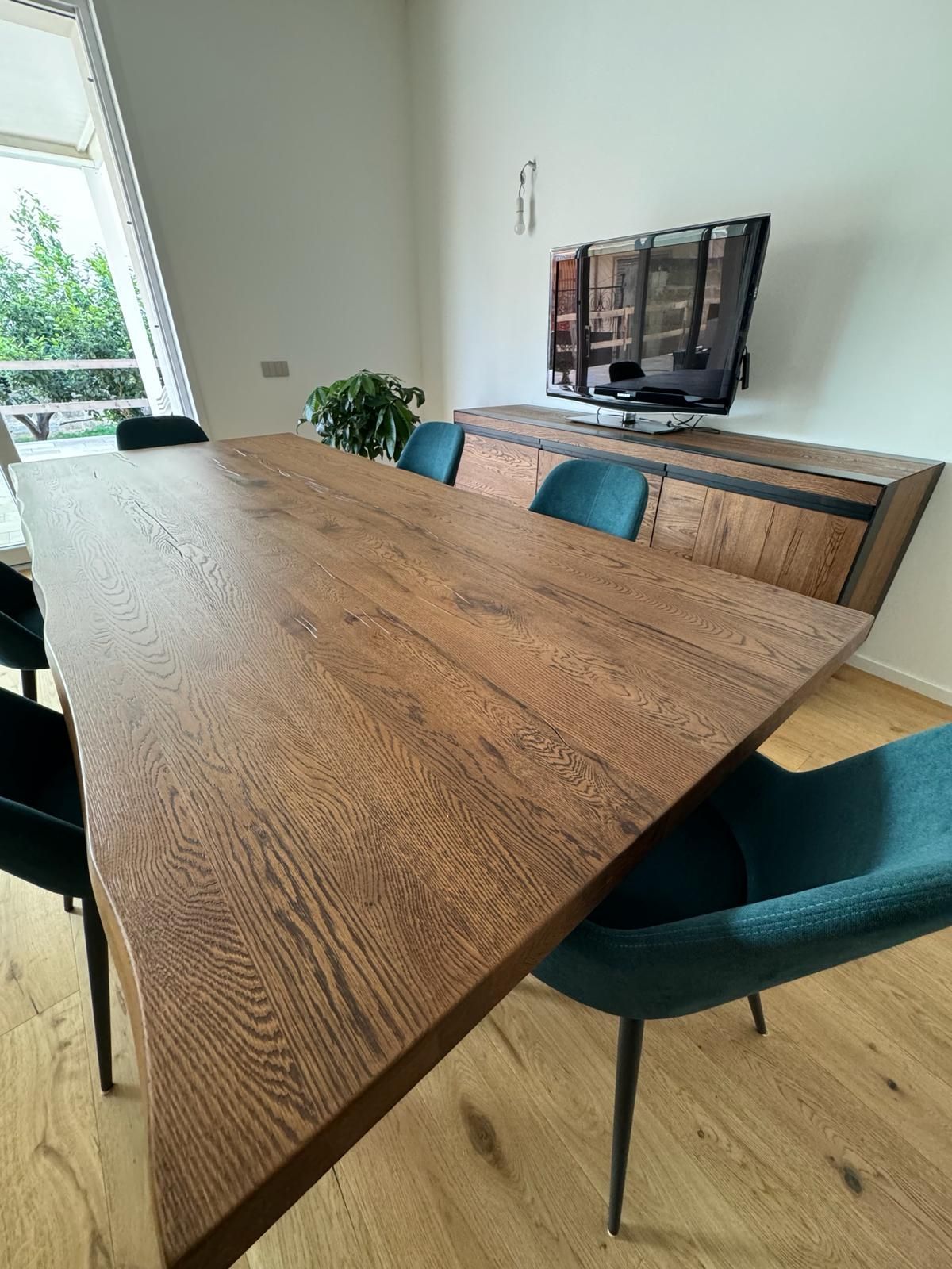 Tavolo da pranzo in legno con sedie color verde acqua, contro una parete con TV e credenza.