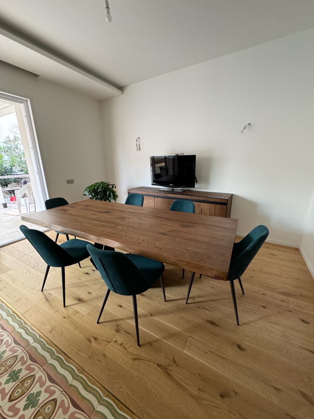 Sala da pranzo con tavolo in legno e sedie color verde acqua, TV su una consolle in legno.