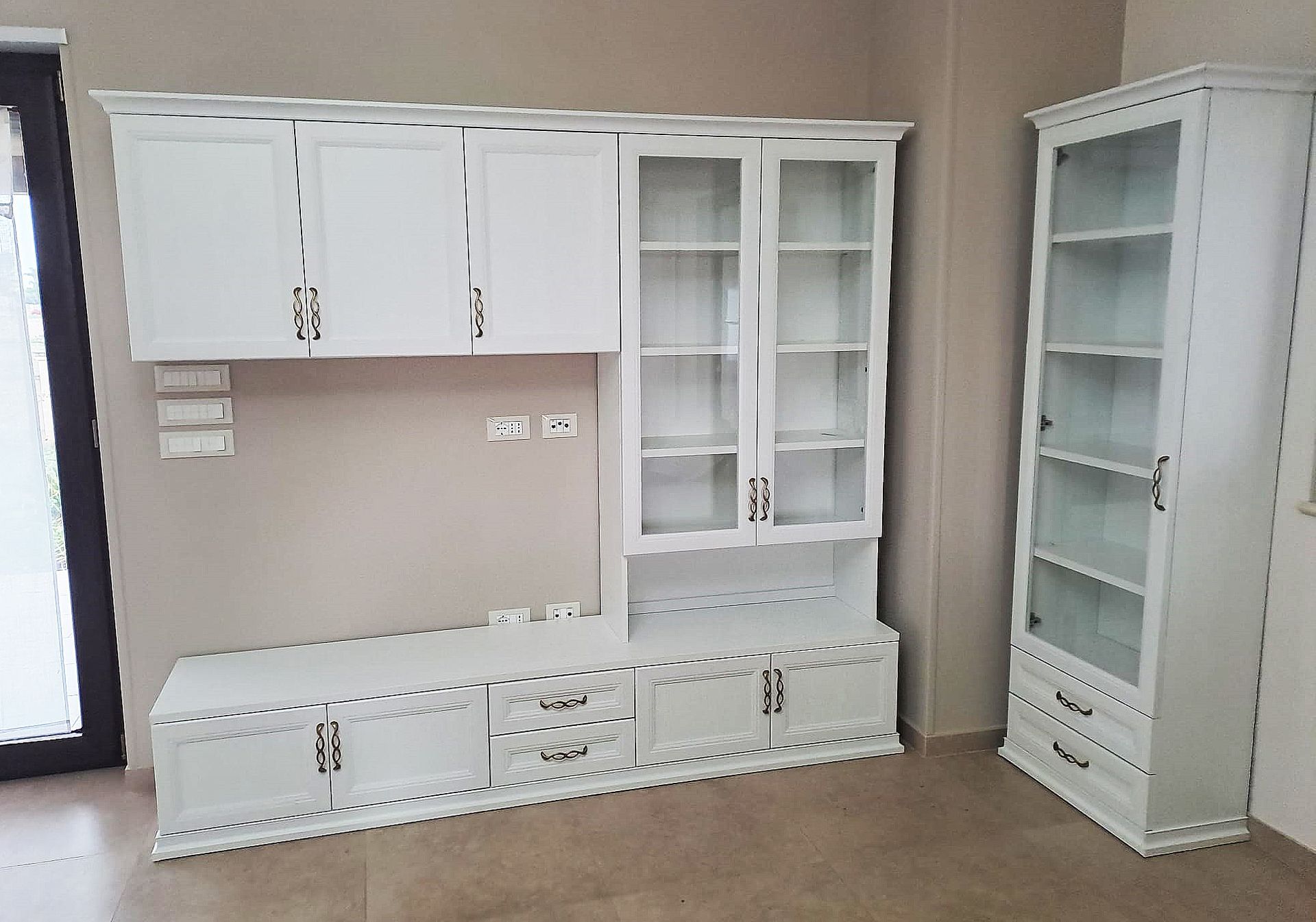 Mobiletto porta TV in legno bianco e vetrina contro una parete neutra.